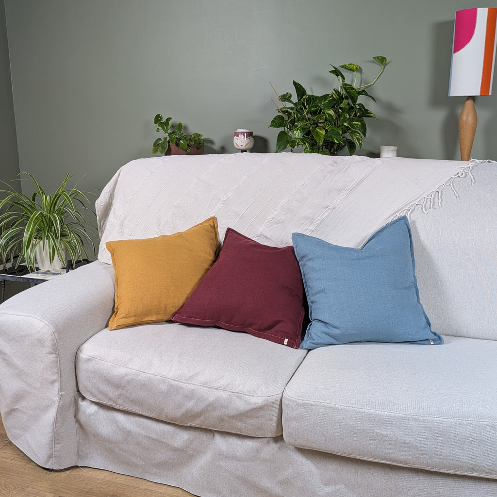 Housses de coussin en lin moutarde, bleu et bordeaux sur canapé blanc - collection Mokiko