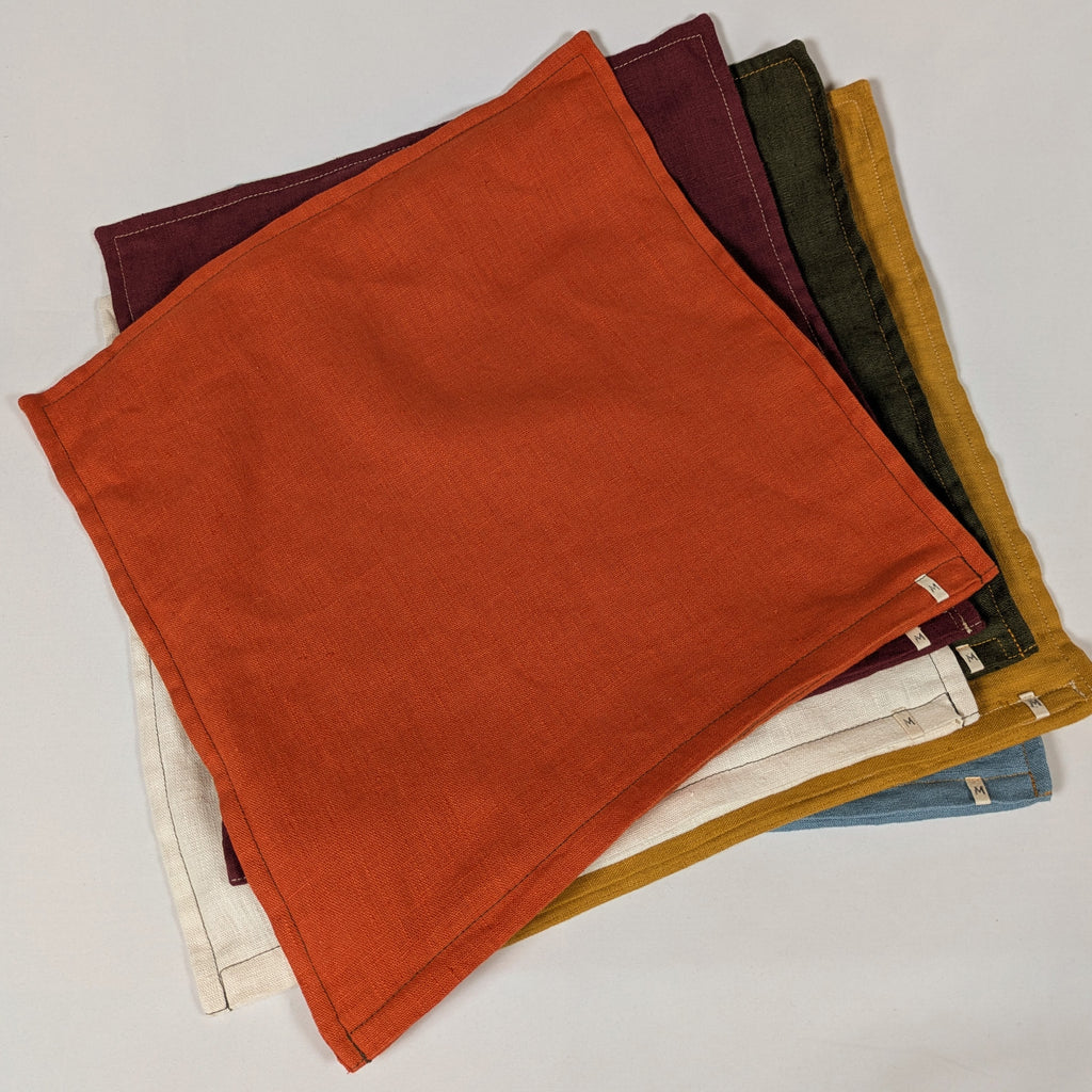 Housses de coussin en lin français empilées, coloris moutarde, bordeaux, orange, kaki, écru et bleu — Mokiko