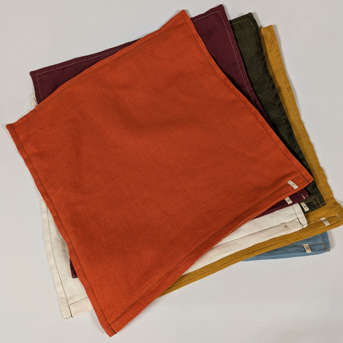 Housses de coussin en lin français empilées, coloris moutarde, bordeaux, orange, kaki, écru et bleu — Mokiko