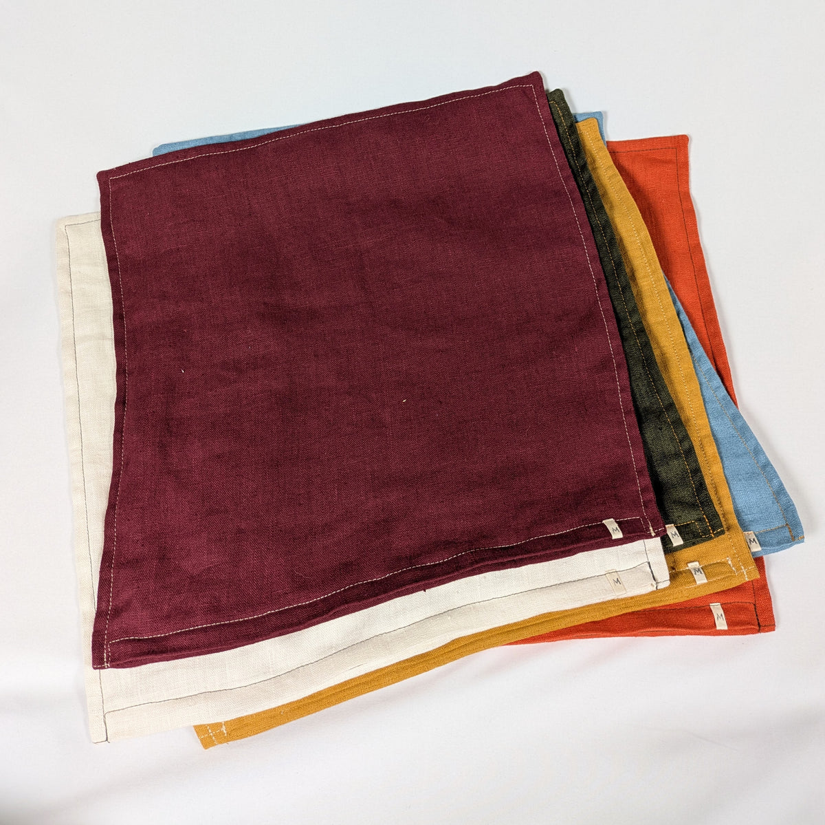 Housses de coussin en lin français empilées, coloris moutarde, bordeaux, terracotta, kaki, écru et bleu — Mokiko