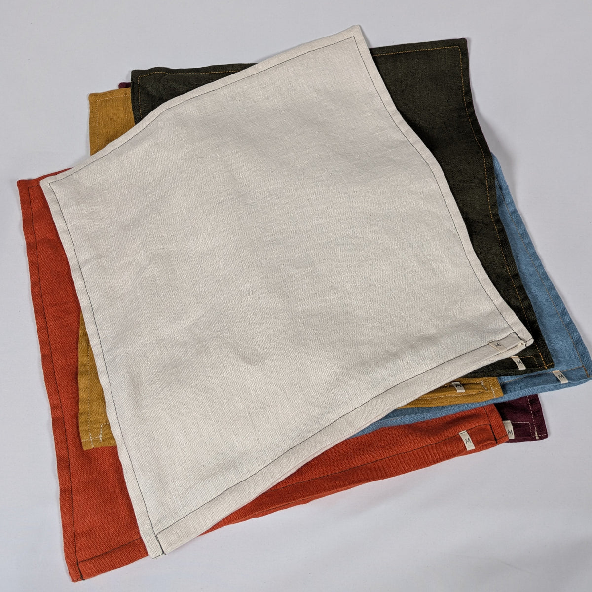 Housses de coussin en lin français empilées, coloris moutarde, bordeaux, terracotta, kaki, écru et bleu — Mokiko