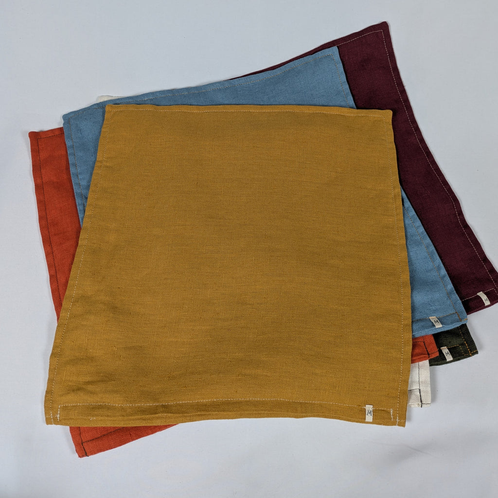 Housses de coussin en lin français empilées, coloris moutarde, bordeaux, terracotta, kaki, écru et bleu — Mokiko