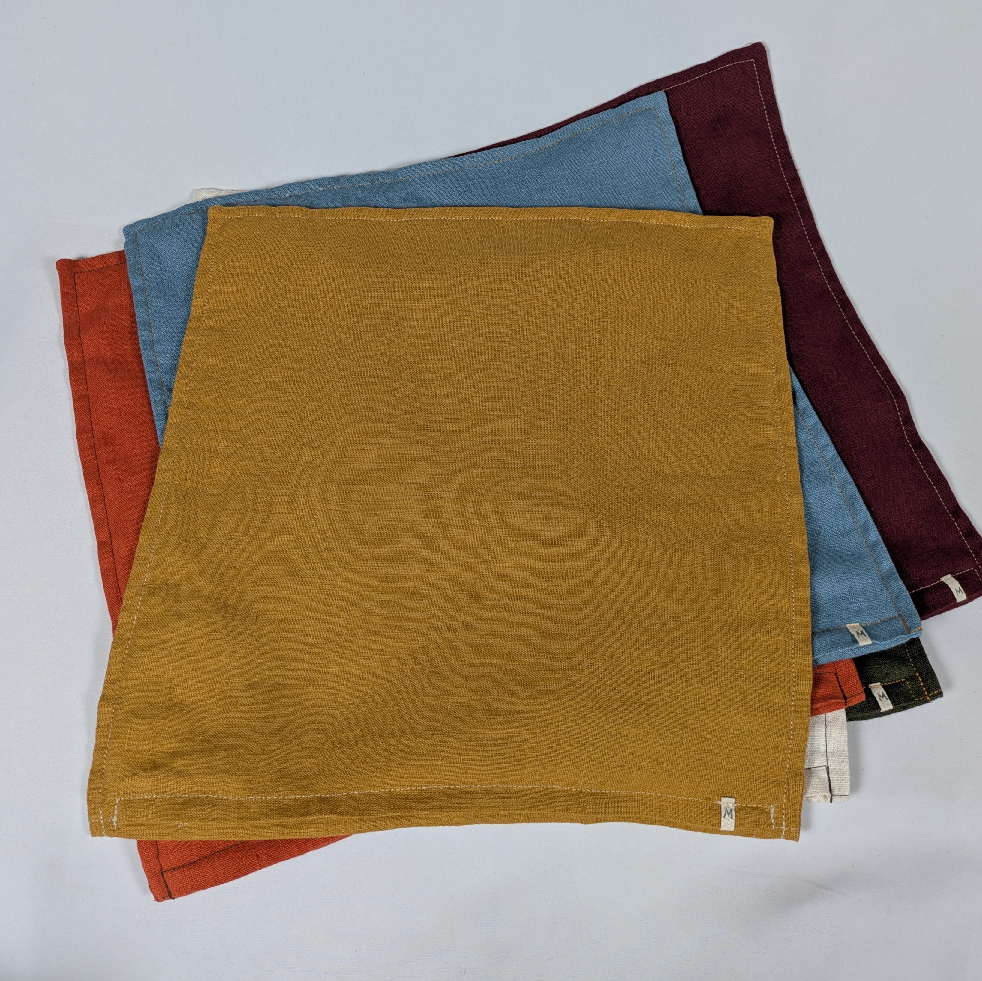 Housses de coussin en lin français empilées, coloris moutarde, bordeaux, terracotta, kaki, écru et bleu — Mokiko