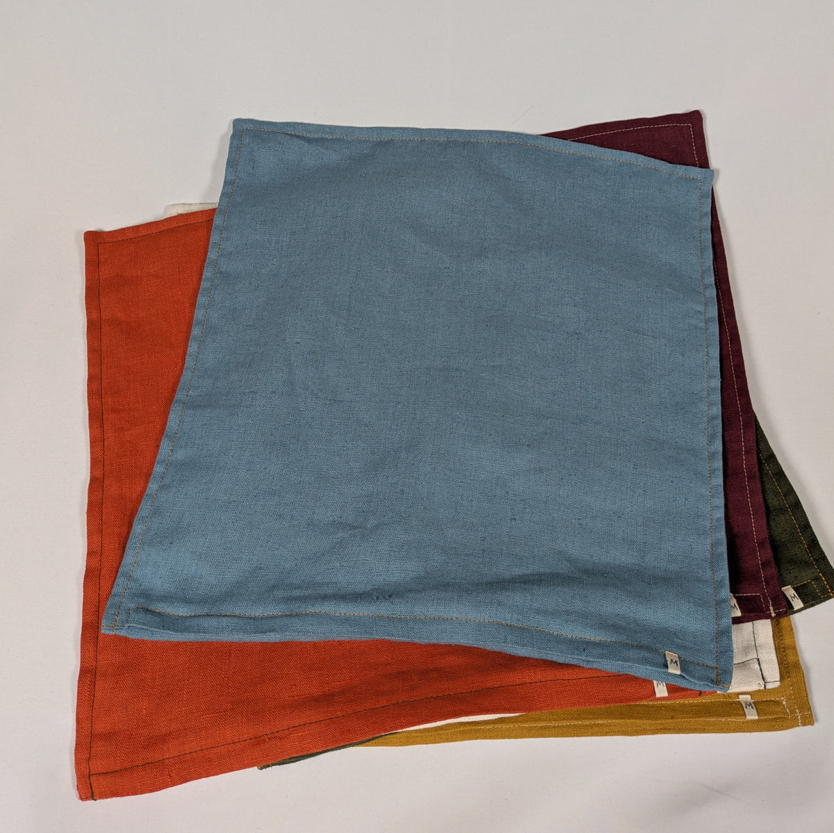 Housses de coussin en lin français empilées, coloris moutarde, bordeaux, terracotta, kaki, écru et bleu — Mokiko